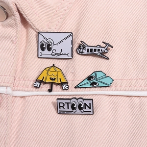 Detail of five cute cartoon enamel pins including envelope and airplane on pink denim fabric