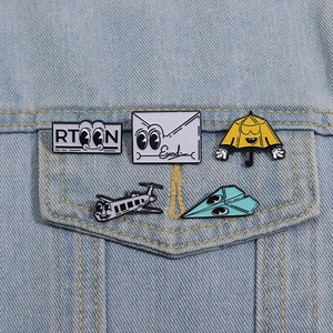 Detail showing five cartoon enamel pins pinned on a light blue denim jacket pocket