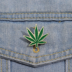 Detail of green maple leaf enamel pin attached to light blue denim jacket pocket