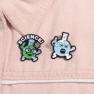 Detail of science enamel pins featuring a green beaker and blue flask on pink denim fabric