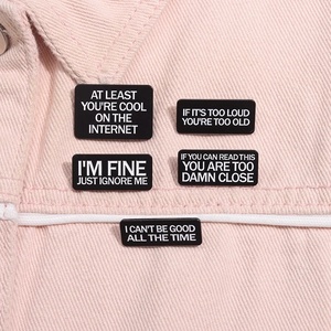 Gros plan de cinq épingles en émail noir avec slogans blancs sur tissu denim rose