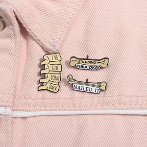 Detailed enamel pins featuring anatomical bones and witty medical puns on pink denim