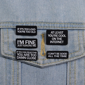 Set of 5 black rectangular metal pins with funny quotes on a blue denim jacket pocket
