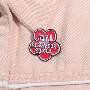 Macro detail of red flower enamel brooch with GIRL READ YOUR BIBLE text on pink denim