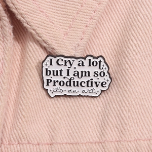 Makro-Detail der Emaille-Brosche mit I Cry a lot Spruch auf rosa strukturiertem Stoff