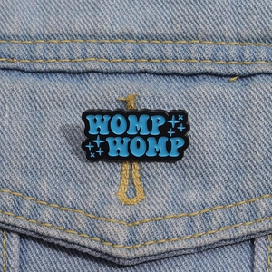 Dettaglio della spilla smaltata blu WOMP WOMP sulla tasca di una giacca denim