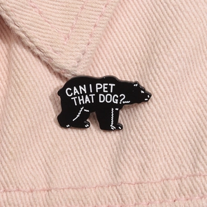 Detail of a black bear enamel pin with funny slogan on pink fabric background