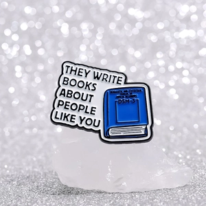 Pin esmaltado de libro azul DSM-5 con texto en inglés sobre piedra mineral blanca