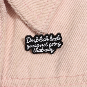 Détail macro d'un pin's en émail noir avec citation blanche sur tissu en jean rose