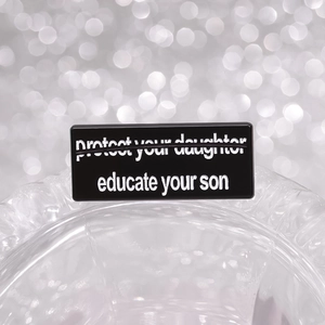 Black enamel pin badge with white text 'educate your son' on a metallic base