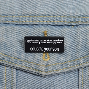 Detail der Educate Your Son Emaille-Anstecknadel an einer blauen Jeansjackentasche