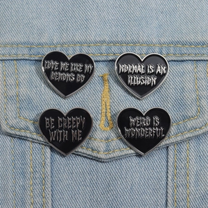 Detail of four black heart-shaped enamel pins with gothic slogans on denim fabric