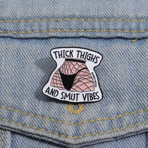 Close-up of Thick Thighs enamel pin with fishnet design on blue denim fabric background