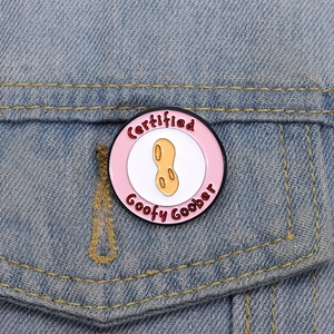 Macro view of pink Goofy Goober peanut enamel pin attached to a blue denim jacket pocket