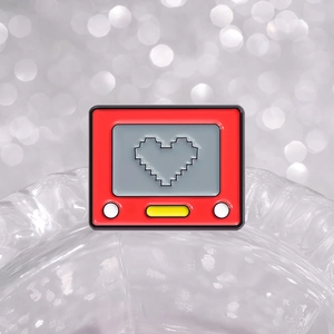 Retro red game console enamel pin with black pixel heart on a silver bokeh background