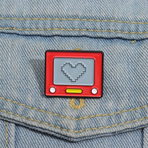 Macro shot of a red retro TV enamel pin with pixel heart on blue denim fabric texture