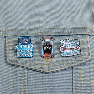Three enamel pins featuring blue bean cans and funny slogans on denim jacket pocket