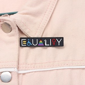 Macro shot of black enamel Equality pin with rainbow symbols on pink denim jacket