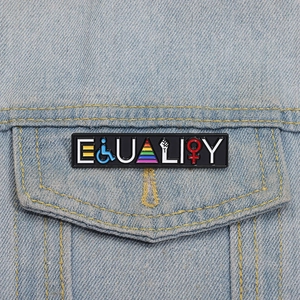 Detail of Equality enamel pin with rainbow symbols on a blue denim jacket pocket