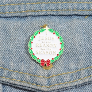 Macro detail of Christmas wreath enamel pin with religious text on denim fabric