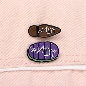 Close-up of enamel ANDY name pins in brown and purple on pink denim fabric background