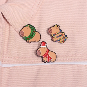 Close-up of three Christmas Capybara enamel pins on pink denim fabric background