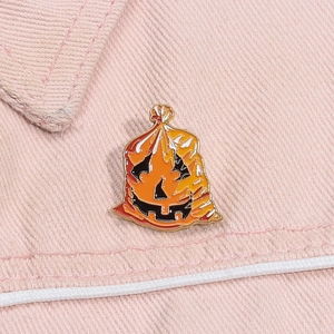 Macro detail of Halloween orange pumpkin enamel pin on pink denim fabric texture