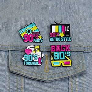 Retro 90's enamel pins with camera and TV icons displayed on a blue denim jacket