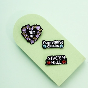 Three creative floral heart enamel pins with bold typography on green display stands