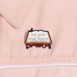 Macro shot of 'Hot Girls Read Horror' open book enamel pin pinned on pink denim jacket
