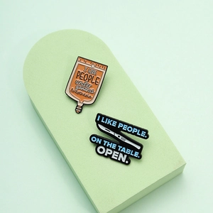 Medical enamel pins with humorous infusion bag and scalpel designs on a green podium