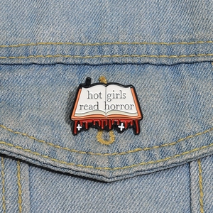 Macro view of 'Hot Girls Read Horror' enamel book brooch pinned on a denim jacket pocket