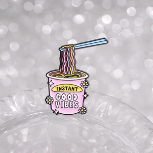 Pink instant noodle enamel pin with blue chopsticks and Good Vibes text badge