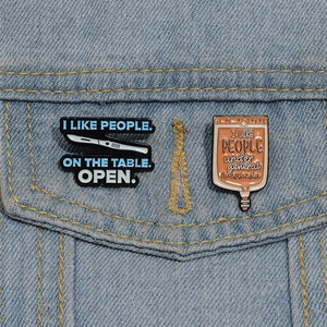 Medical enamel pins on denim jacket featuring scalpel and IV drip bag designs