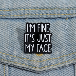 Macro detail of 'I'M FINE IT'S JUST MY FACE' enamel pin on denim fabric