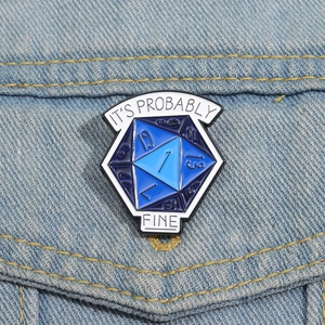 Detail of D20 dice enamel pin with It's Probably Fine slogan on blue denim jacket