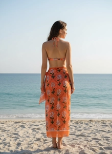 Detail view of orange floral sarong and halter swimsuit against a tropical beach background