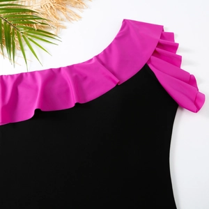 Detail of black one-shoulder swimsuit featuring vibrant rose red ruffle trim and sleek fabric