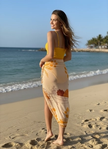 Detail of yellow backless swimsuit with a translucent floral sarong on a beach