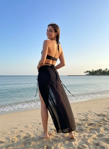 Three-piece black bikini set with high-slit sheer beach sarong cover-up on sandy beach