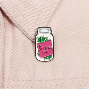 Détail de l'épingle en émail Douchebag Jar fixée sur une veste en denim rose pastel