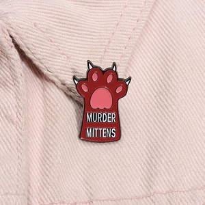 Detailed close-up of a red cat paw enamel pin with Murder Mittens text on pink denim