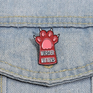 Detail of red cat paw enamel pin with Murder Mittens text on blue denim jacket