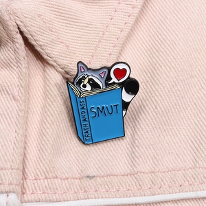 Vue détaillée d'un pin's en émail de raton laveur lisant un livre sur du denim rose