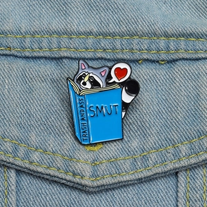 Détail d'un pin's en émail raton laveur lisant un livre sur une veste en denim bleu
