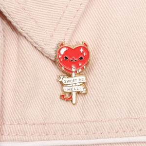 Dettaglio della spilla in smalto a cuore diavolo con testo Sweet As Hell su denim rosa