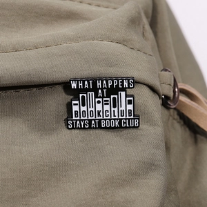 Détail d'un pin's émaillé Book Club avec lettrage sur un sac à dos en toile verte