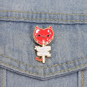 Dettaglio della spilla smaltata lecca-lecca cuore diavolo rosso su denim