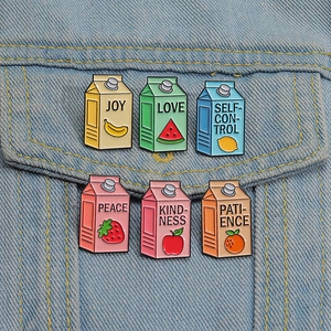 Detail of six colorful fruit milk carton enamel pins pinned on a blue denim jacket pocket