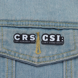 Detail of funny CRS and CSI enamel pins attached to blue denim fabric texture